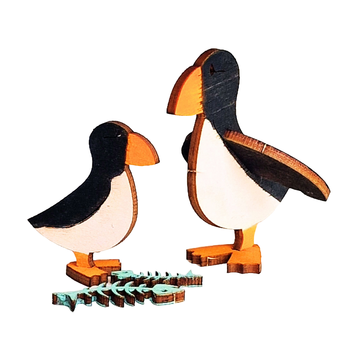 Two painted wooden puffin models in black, white and orange beside two blue fish skeletons, from the Puffin Wooden Craft Kit