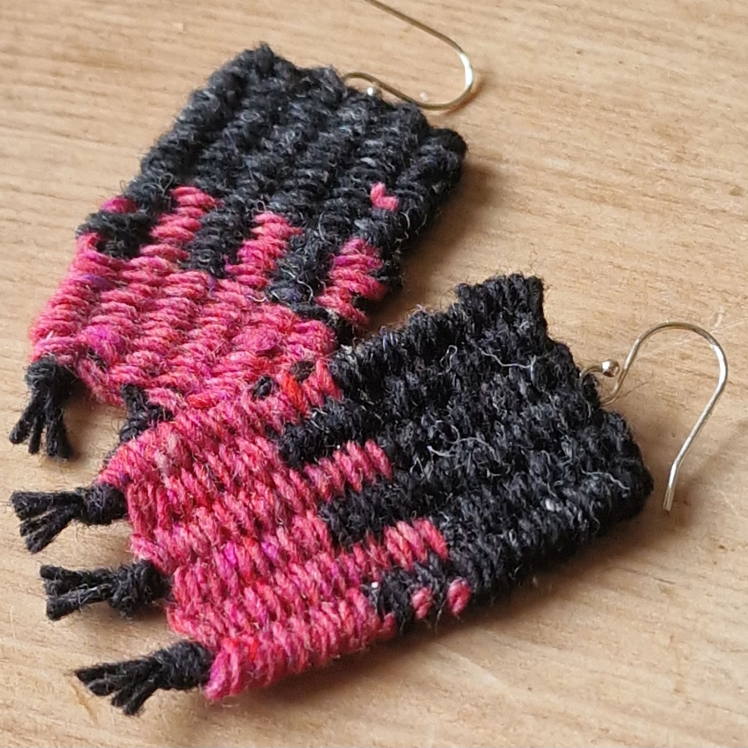 Pair of pink and black woven earrings on a wooden surface
