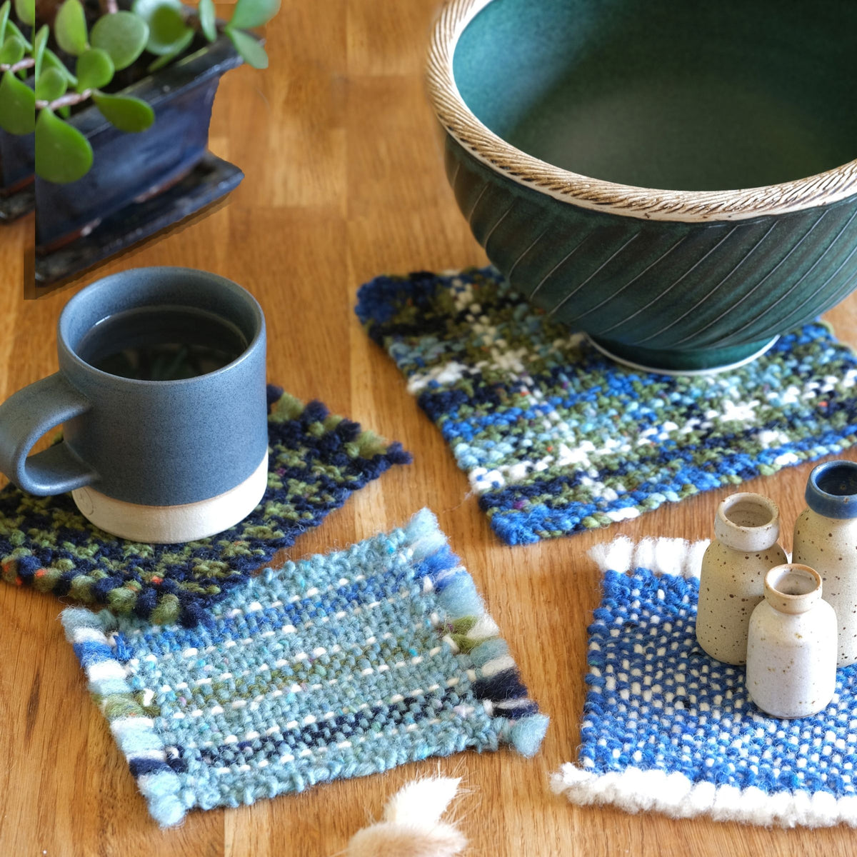 Lakeshore handwoven tweed coasters in blue, green and cream, styled with ceramics on a wooden table.